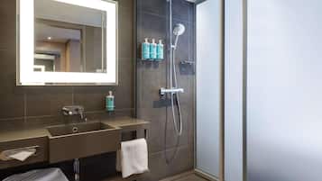 A modern bathroom with a large mirror, a sink, a shower, and toiletries.
