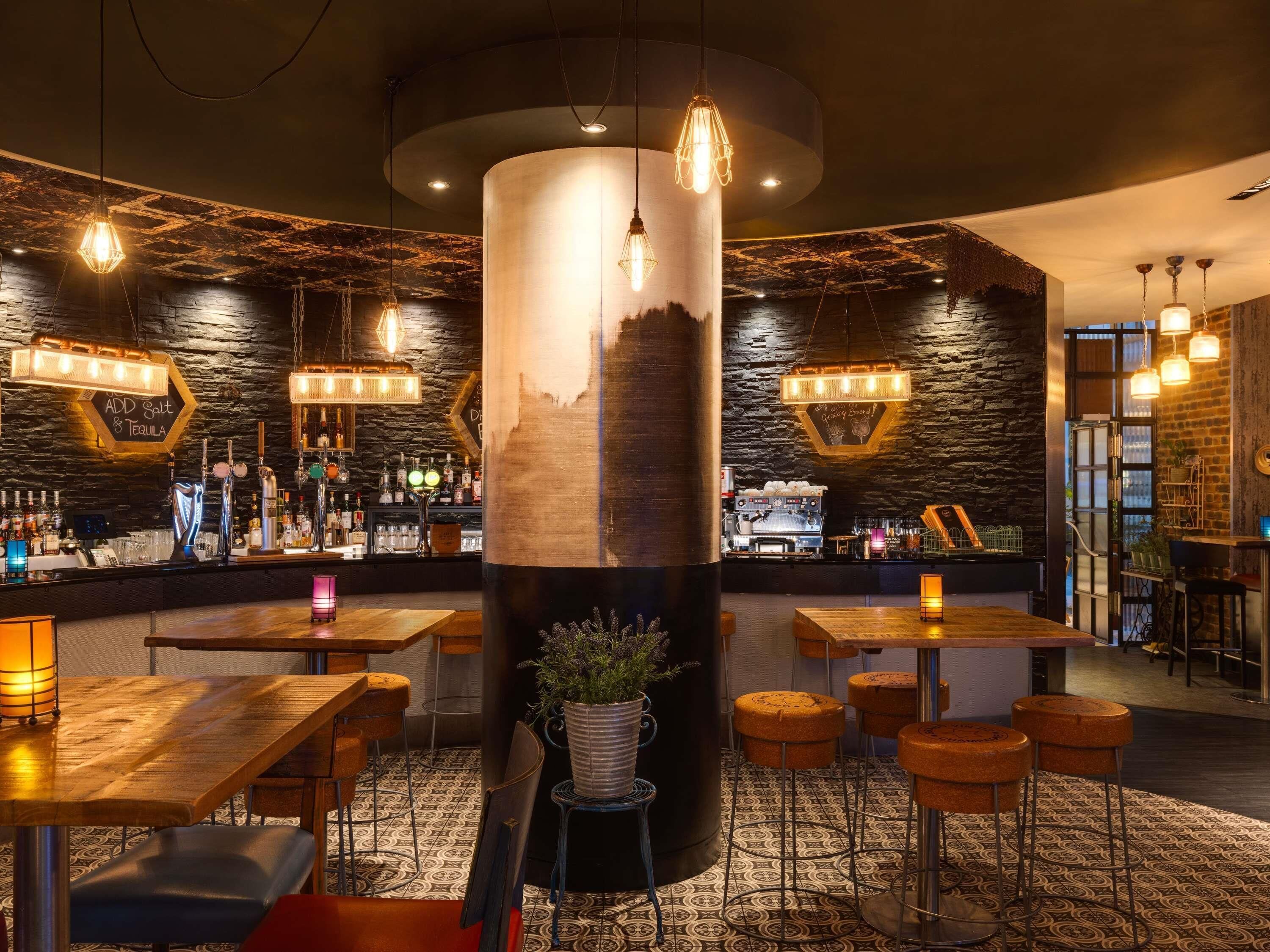 A bar area with a central column, bar stools, tables, and a coffee machine.