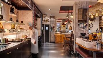 A chef preparing food in a well-lit kitchen with a coffee station and herb display.