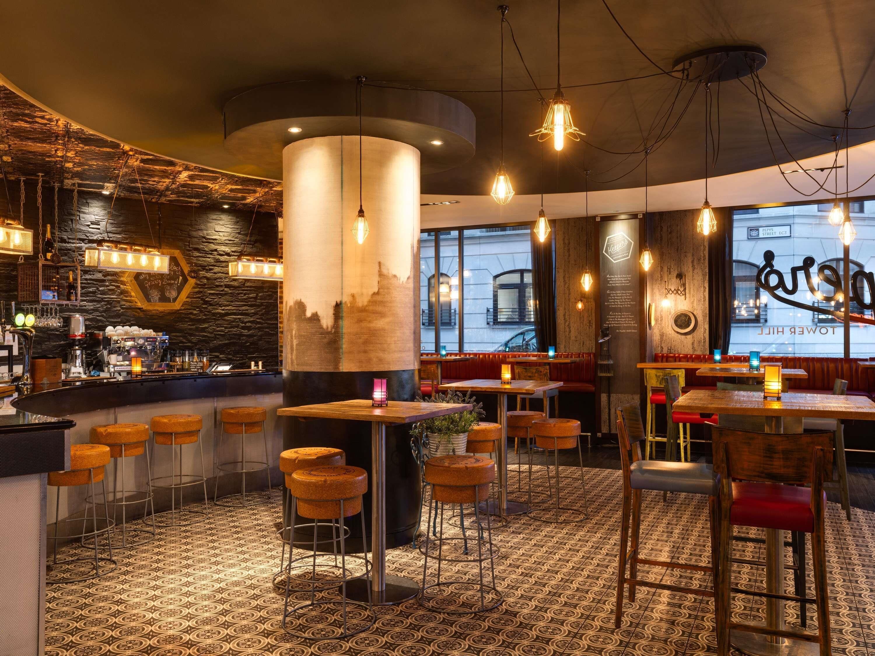 A restaurant interior with high tables, stools, hanging lights, a bar area, and a city view through large windows.