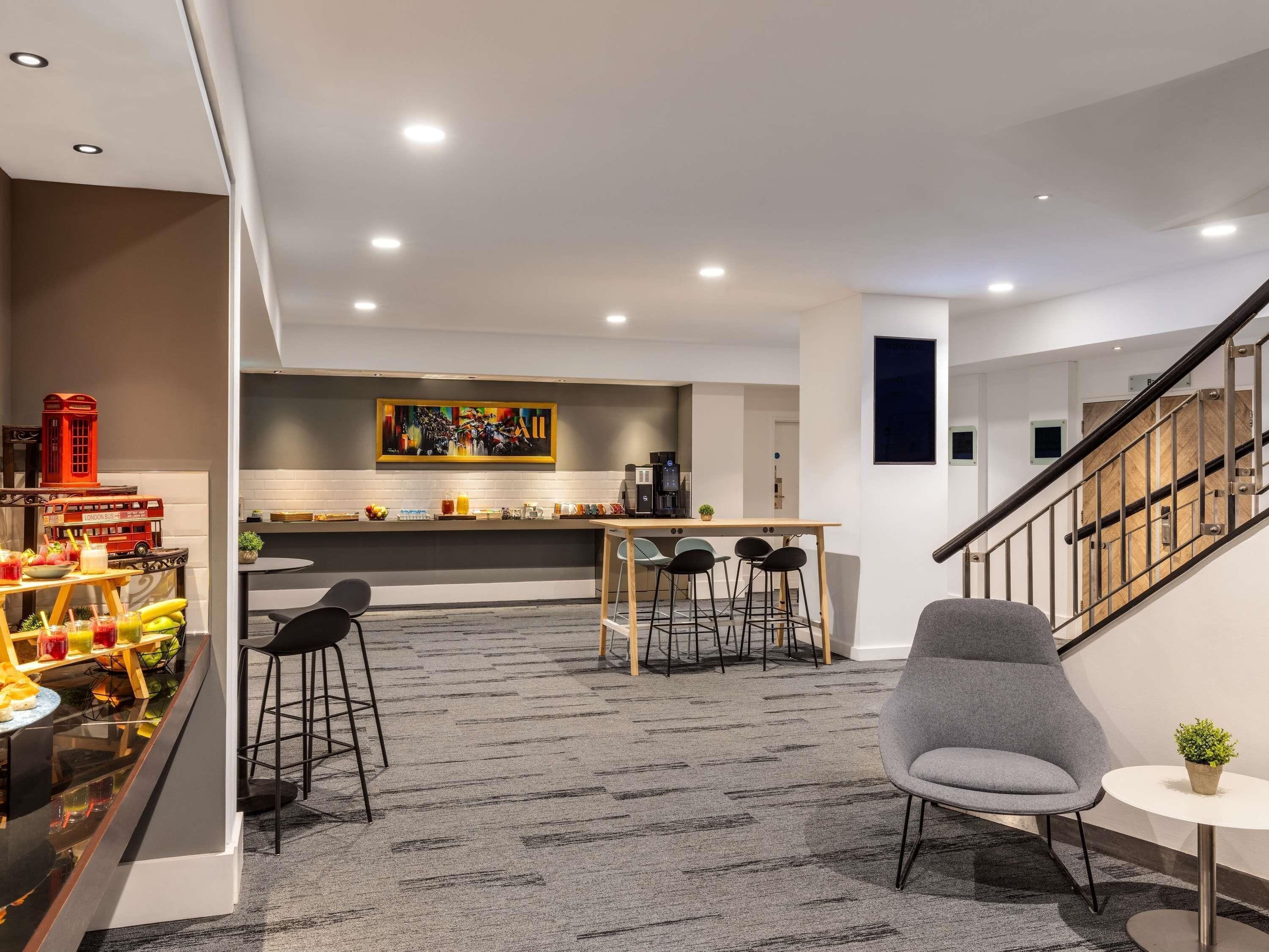 En modern hotellobby med en bardisk, sittplatser och en trappa.