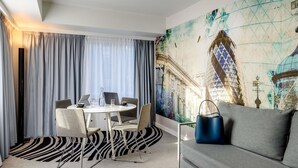 A hotel room with a round table, two chairs, a sofa, a zebra-patterned rug, and a large wall mural.