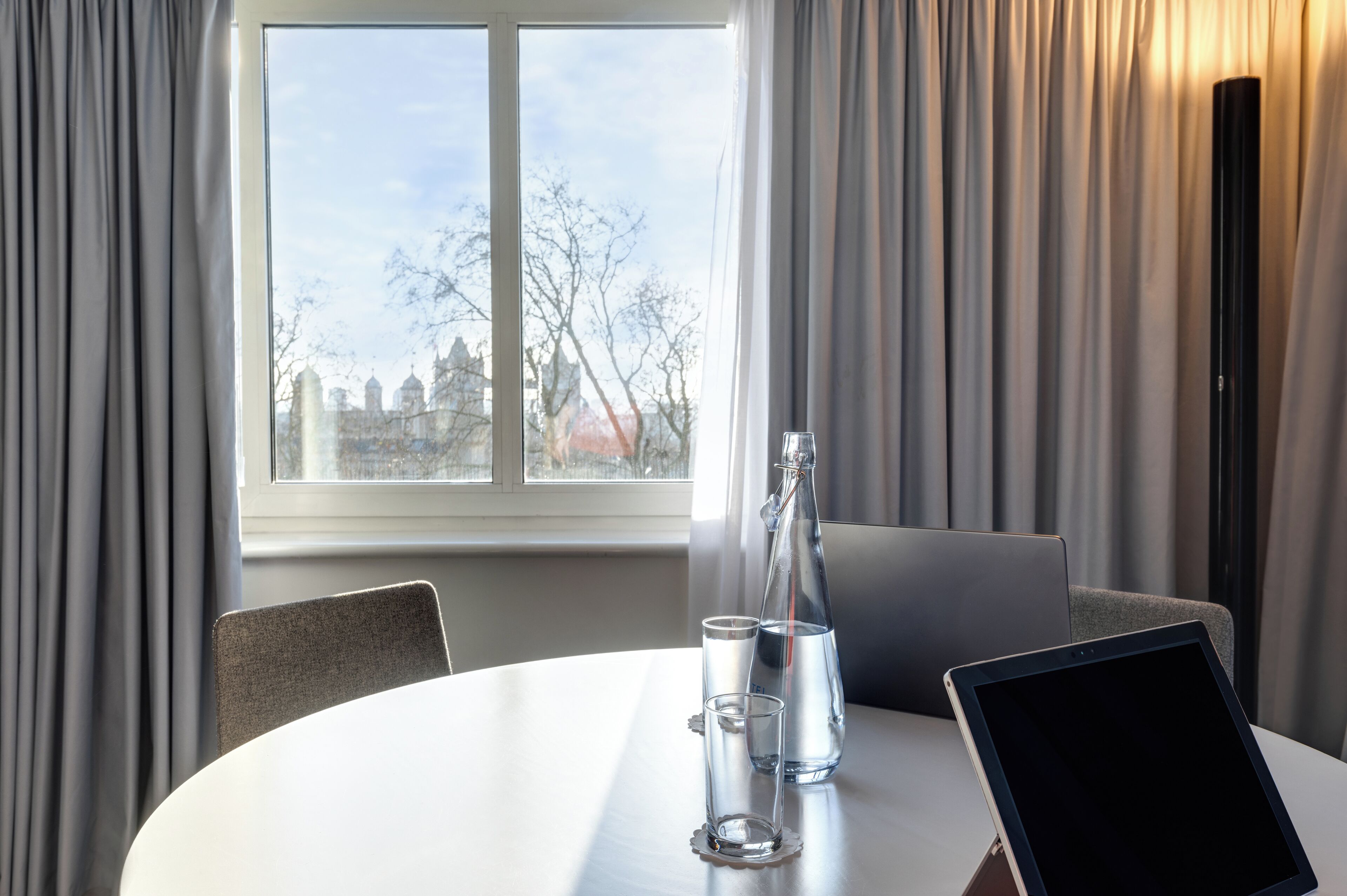 A modern room with a round table, a laptop, two glasses, and a bottle.