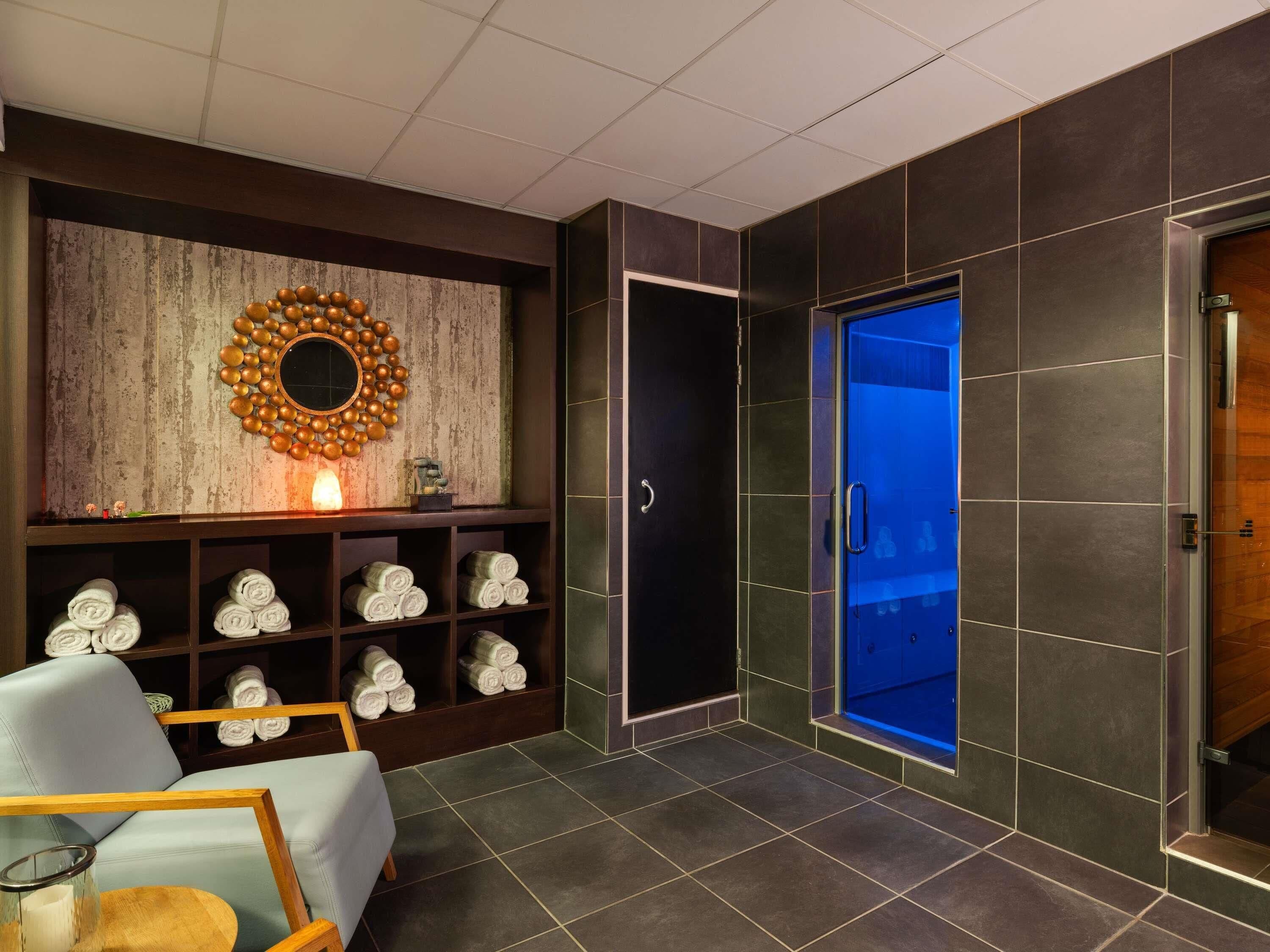 Casa de banho moderna com um espelho grande, um porta-toalhas, uma cabine de duche com iluminação azul e uma porta de madeira.