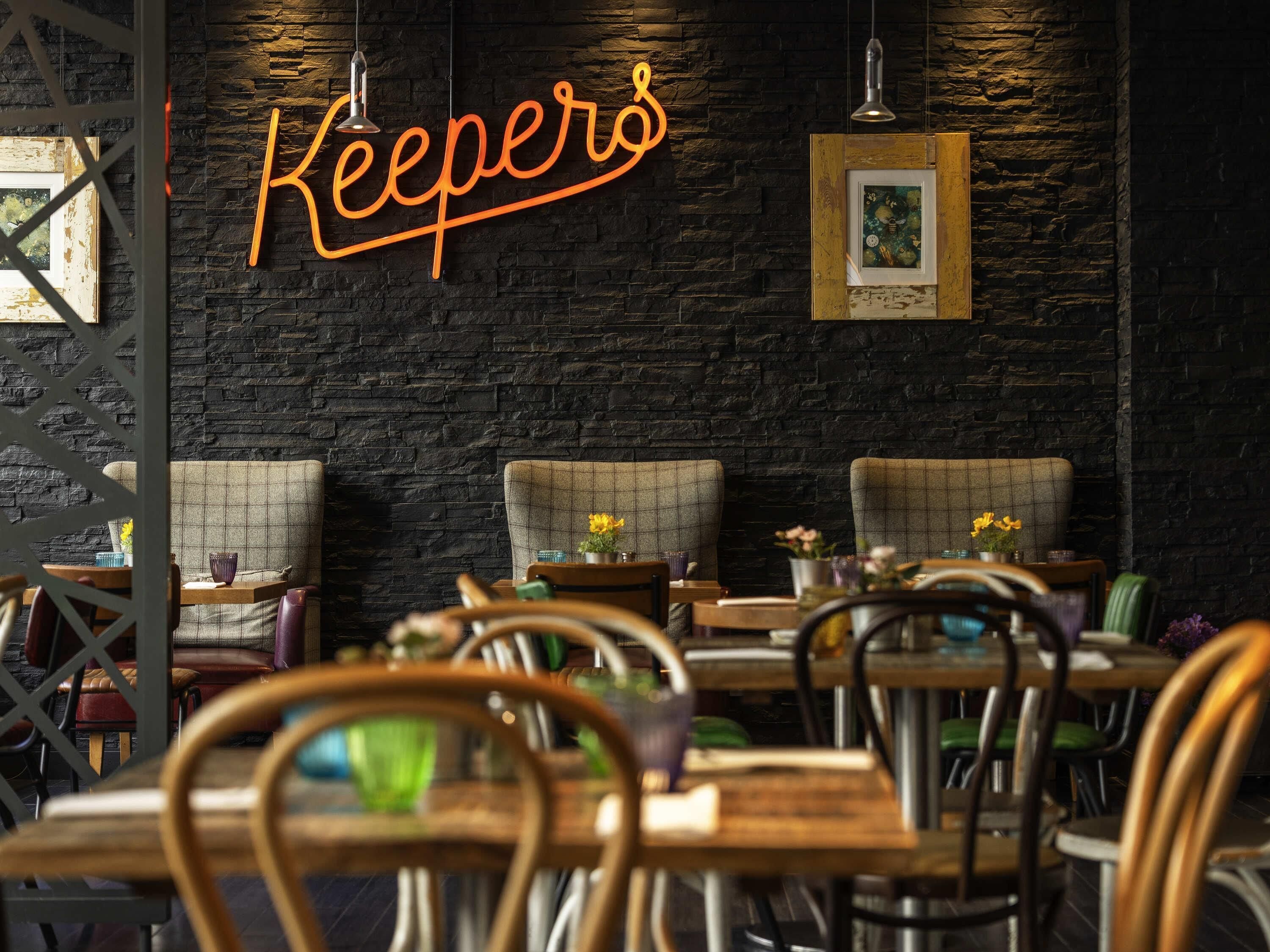 Un interior de restaurante con un letrero de neón que dice 'Keepers', mesas y sillas de madera.