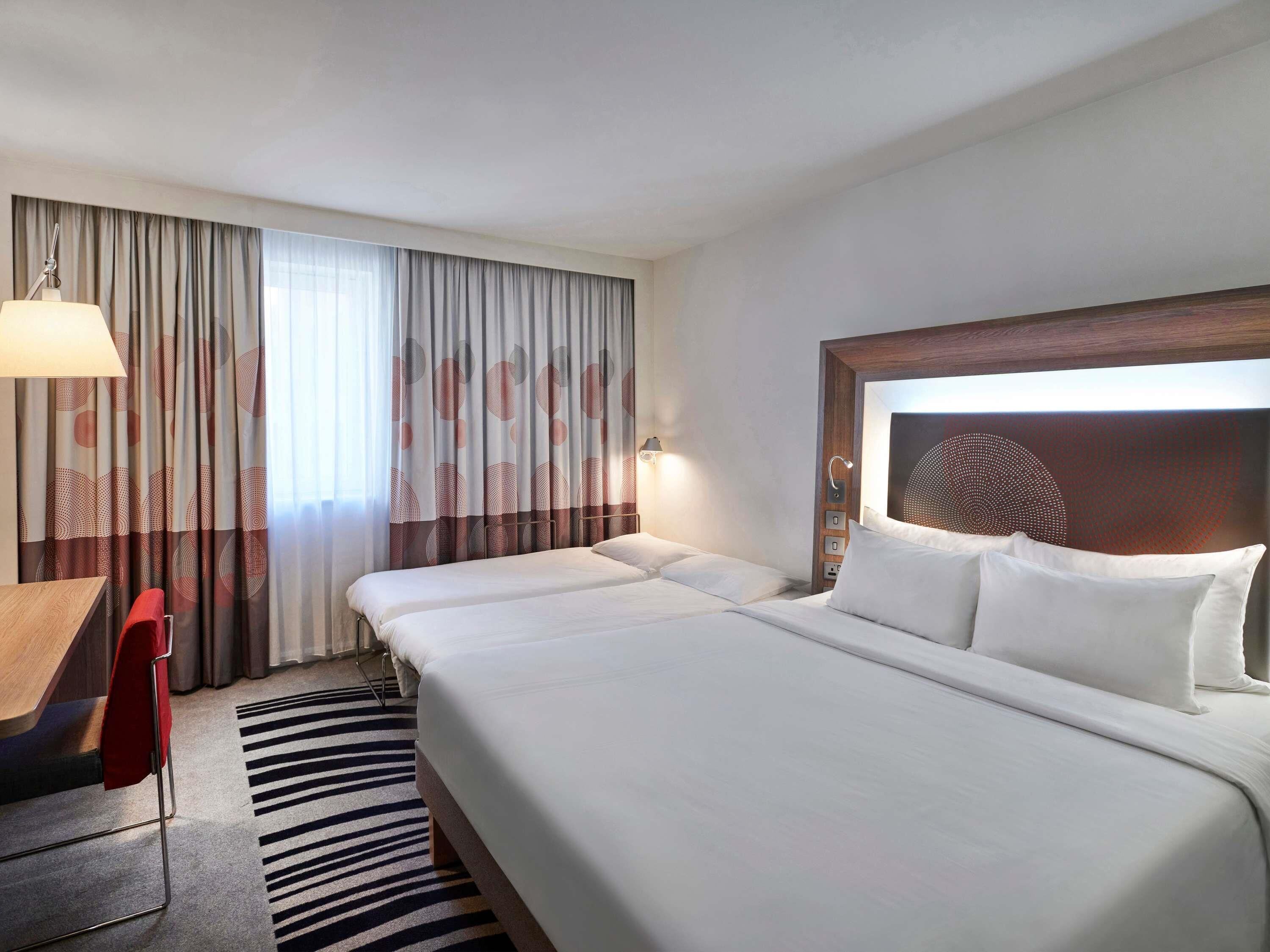 Habitación de hotel con una cama grande, un escritorio, una silla y una cortina estampada.