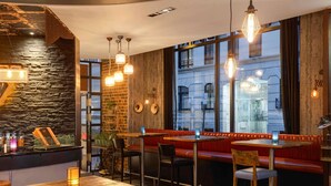 A restaurant interior with a stone wall, wooden tables, leather booths, and hanging light fixtures.
