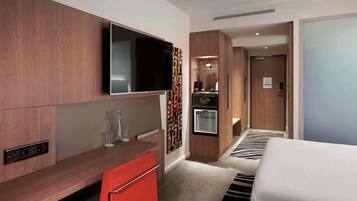 Quarto de hotel com cama, mesa com cadeira, televisão, minibar e porta que dá para outro aposento.