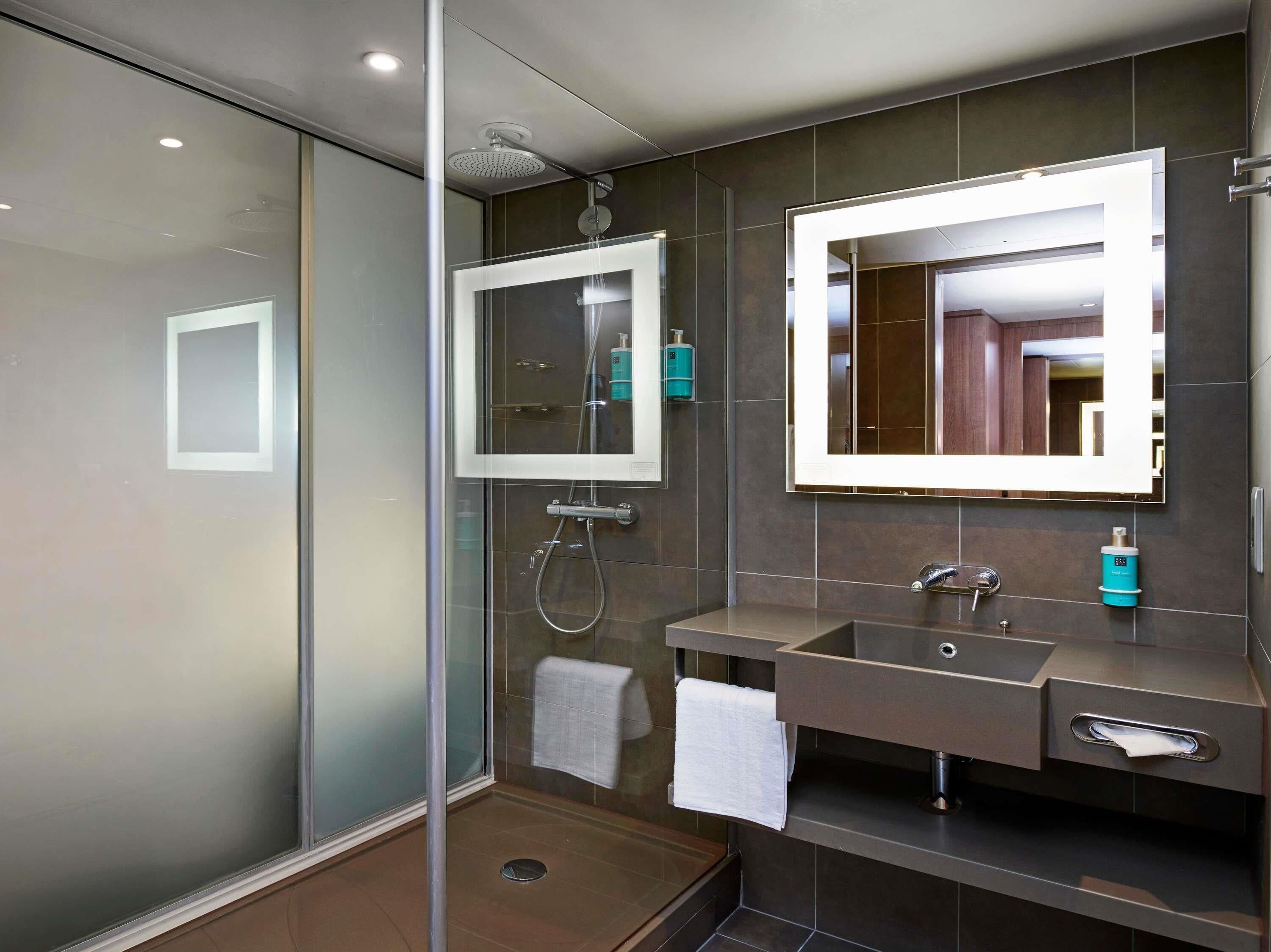 A modern bathroom with a glass shower enclosure, a large mirror, and a vanity with a sink and towel rack.
