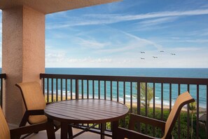 A balcony with a round table and chairs, overlooking a beach with waves and a clear sky. - Vistana Beach Club (Jensen Beach)