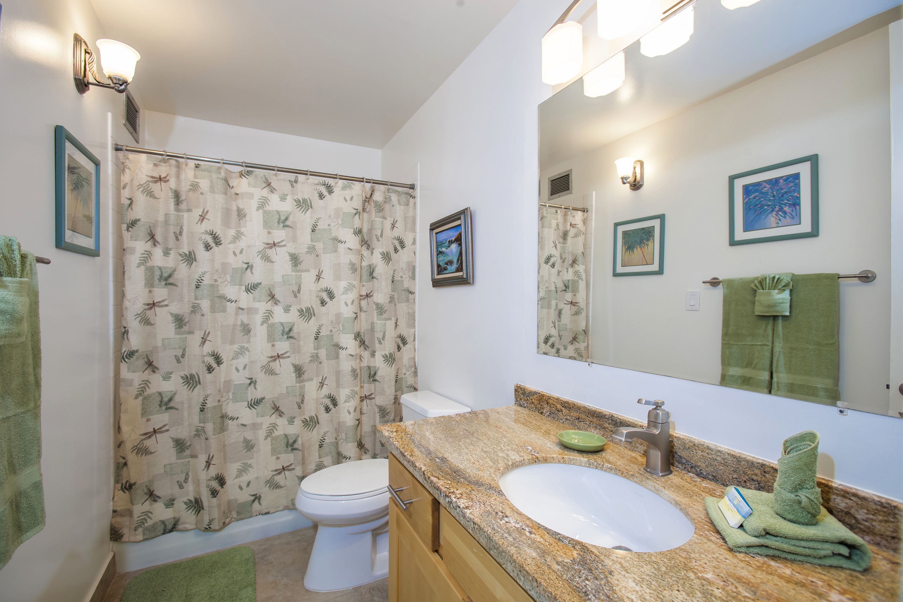 A bathroom with a shower curtain, toilet, sink, and mirror.