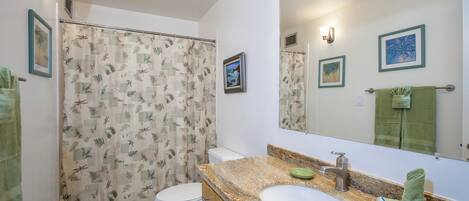 A bathroom with a shower curtain, toilet, sink, and mirror.
