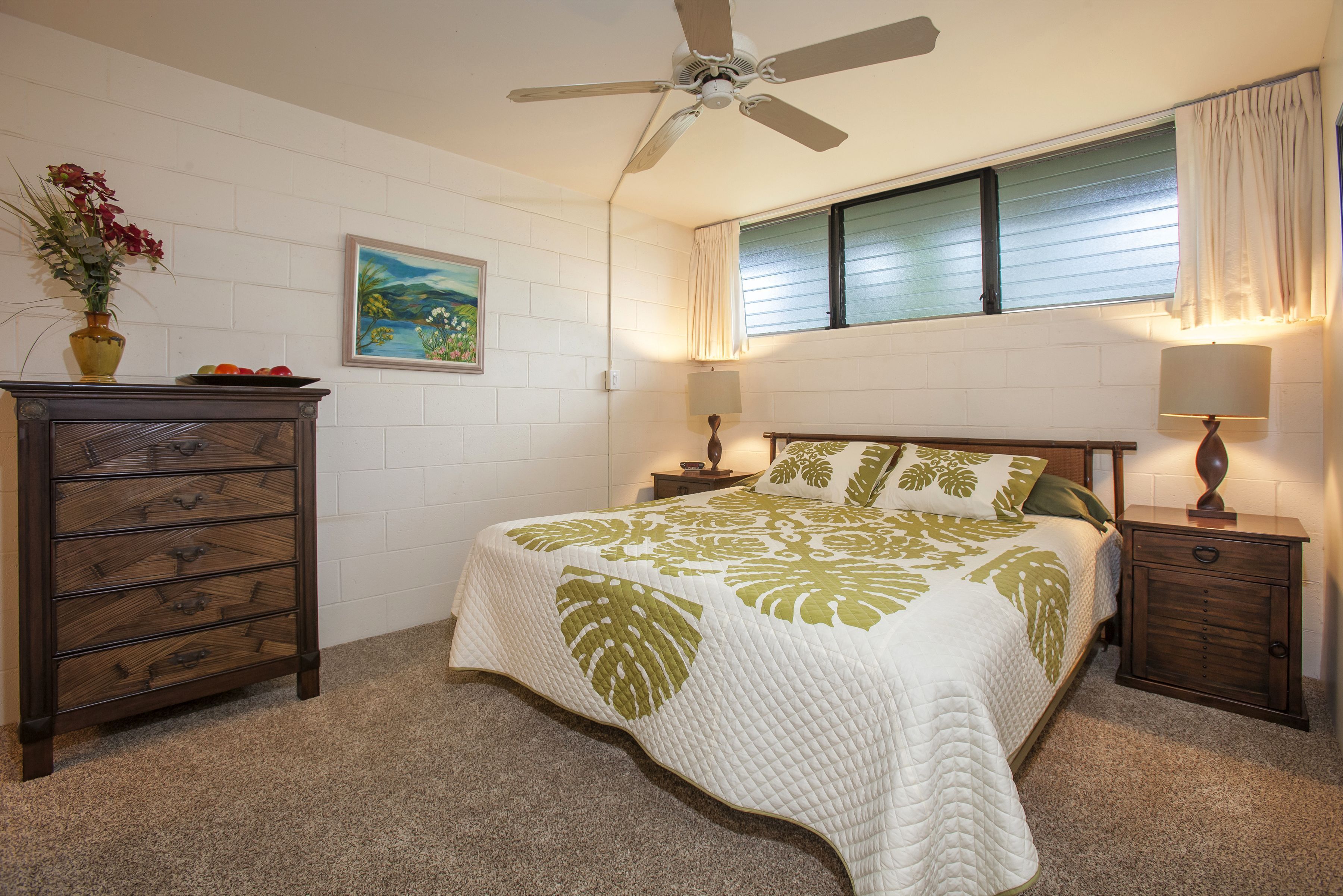 A bedroom with a bed, dresser, nightstands, lamps, a ceiling fan, a window with blinds, and a painting on the wall.