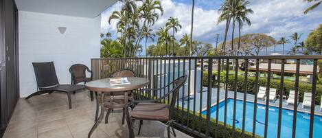 A balcony with a view of a swimming pool, palm trees, and a clear sky.