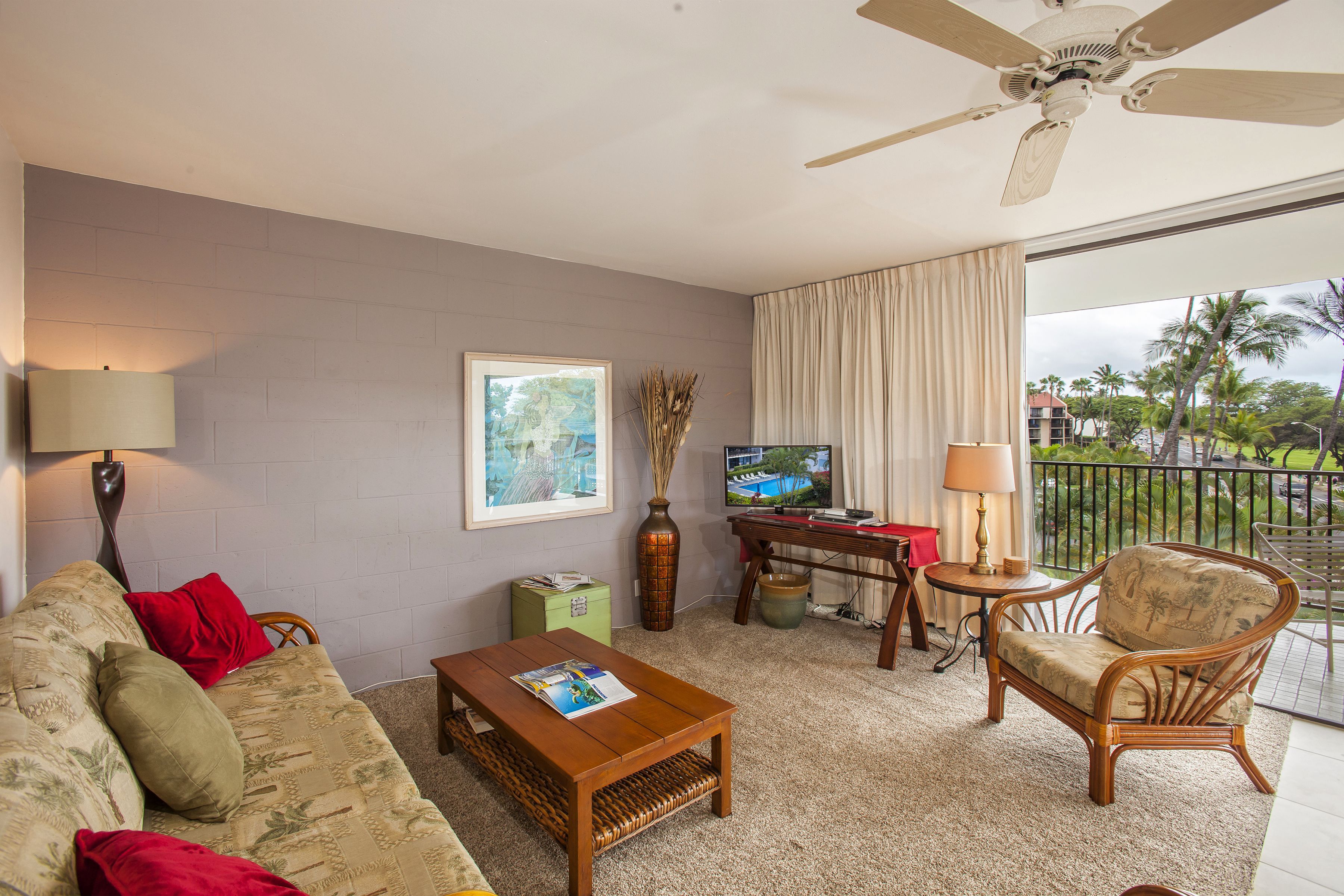 A living room with a sofa, coffee table, and armchairs, a television, a lamp, and a framed picture on the wall.
