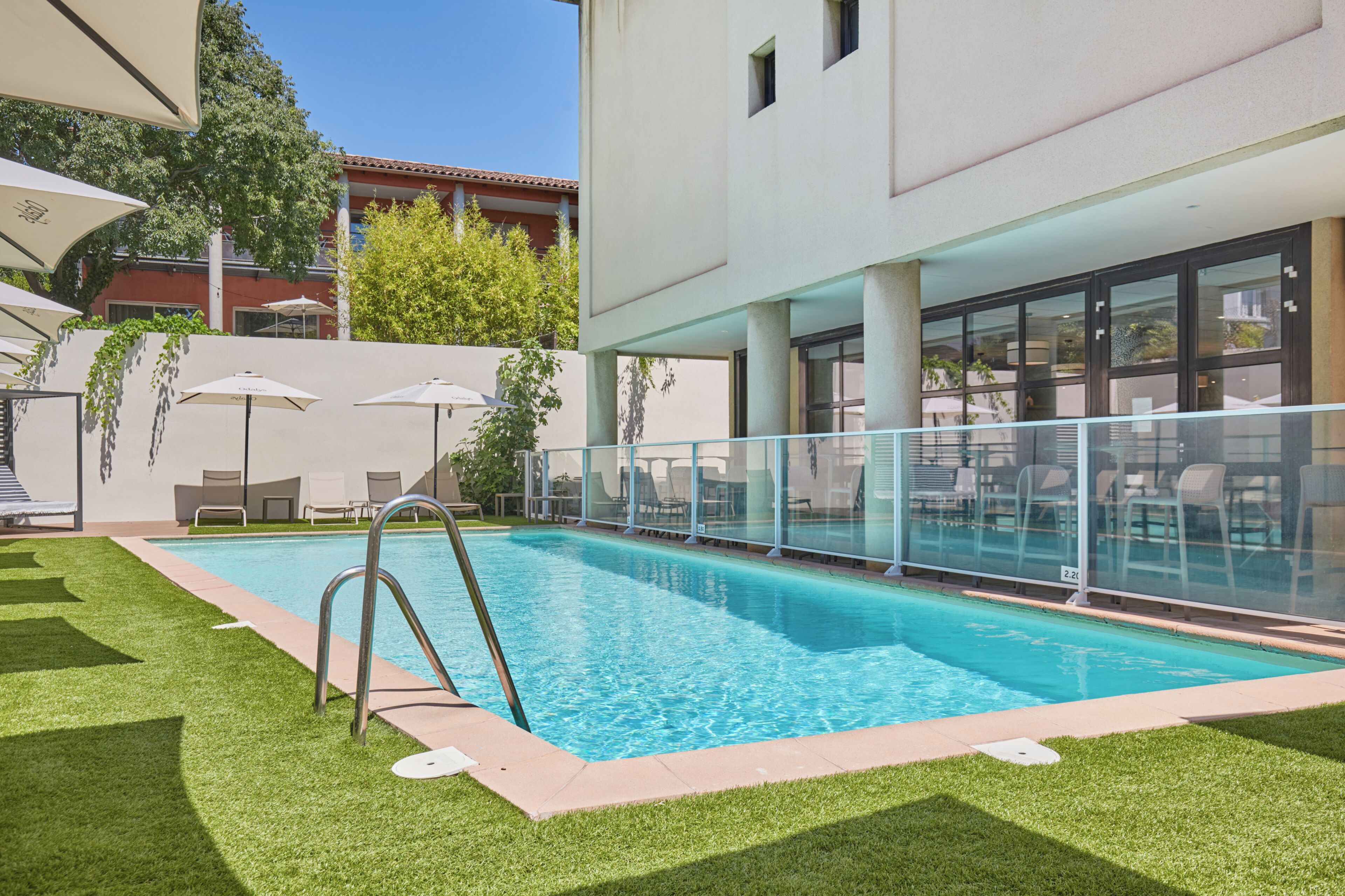 A swimming pool with a glass railing, surrounded by artificial grass and lounge chairs.