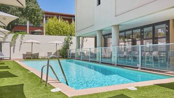 A swimming pool with a glass railing, surrounded by artificial grass and lounge chairs.
