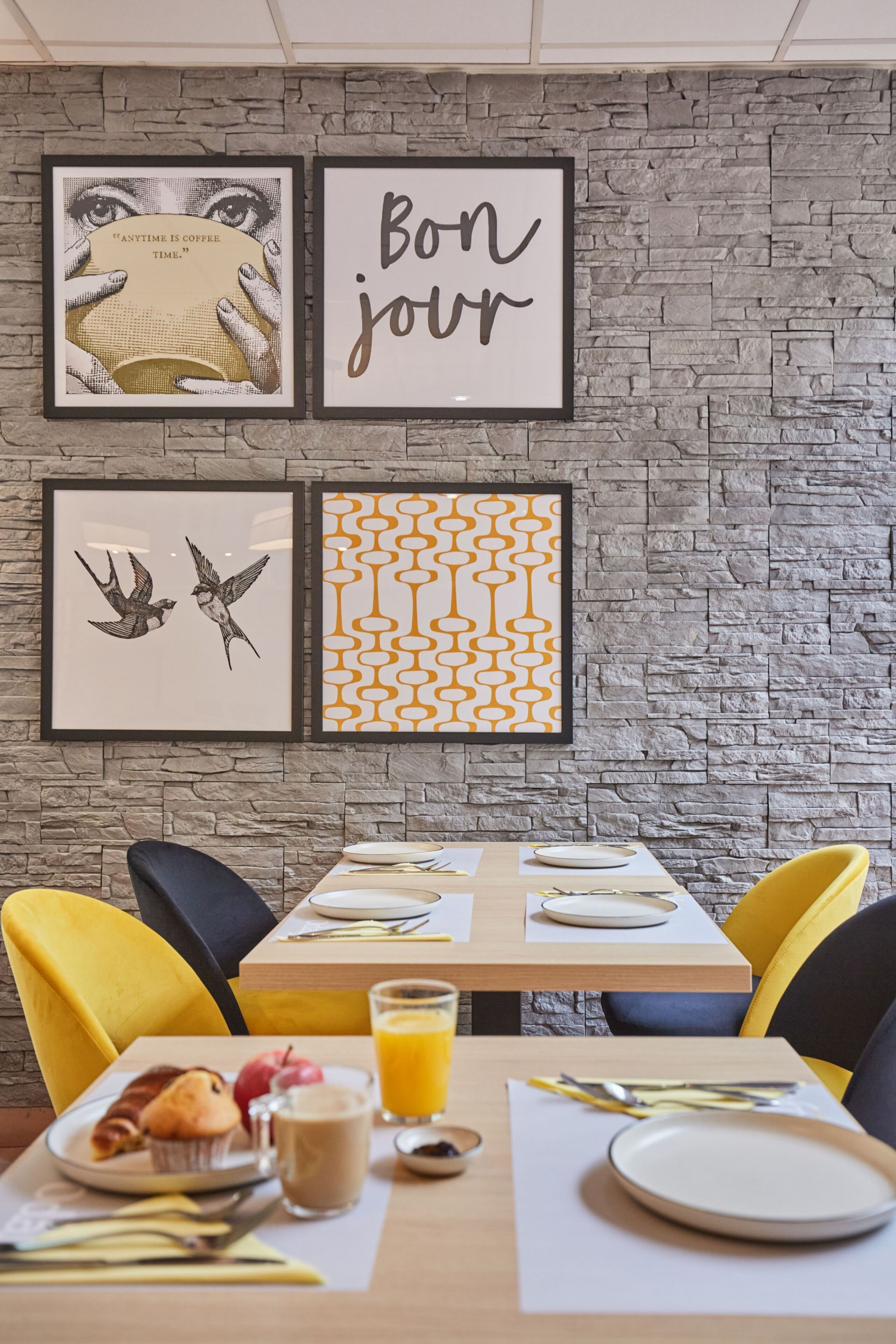 Un comedor con pared de piedra, cuadros enmarcados y una mesa dispuesta para el desayuno.
