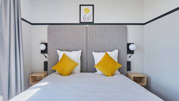 A modern hotel room with a large bed, two bedside tables, and a headboard with a framed picture above.