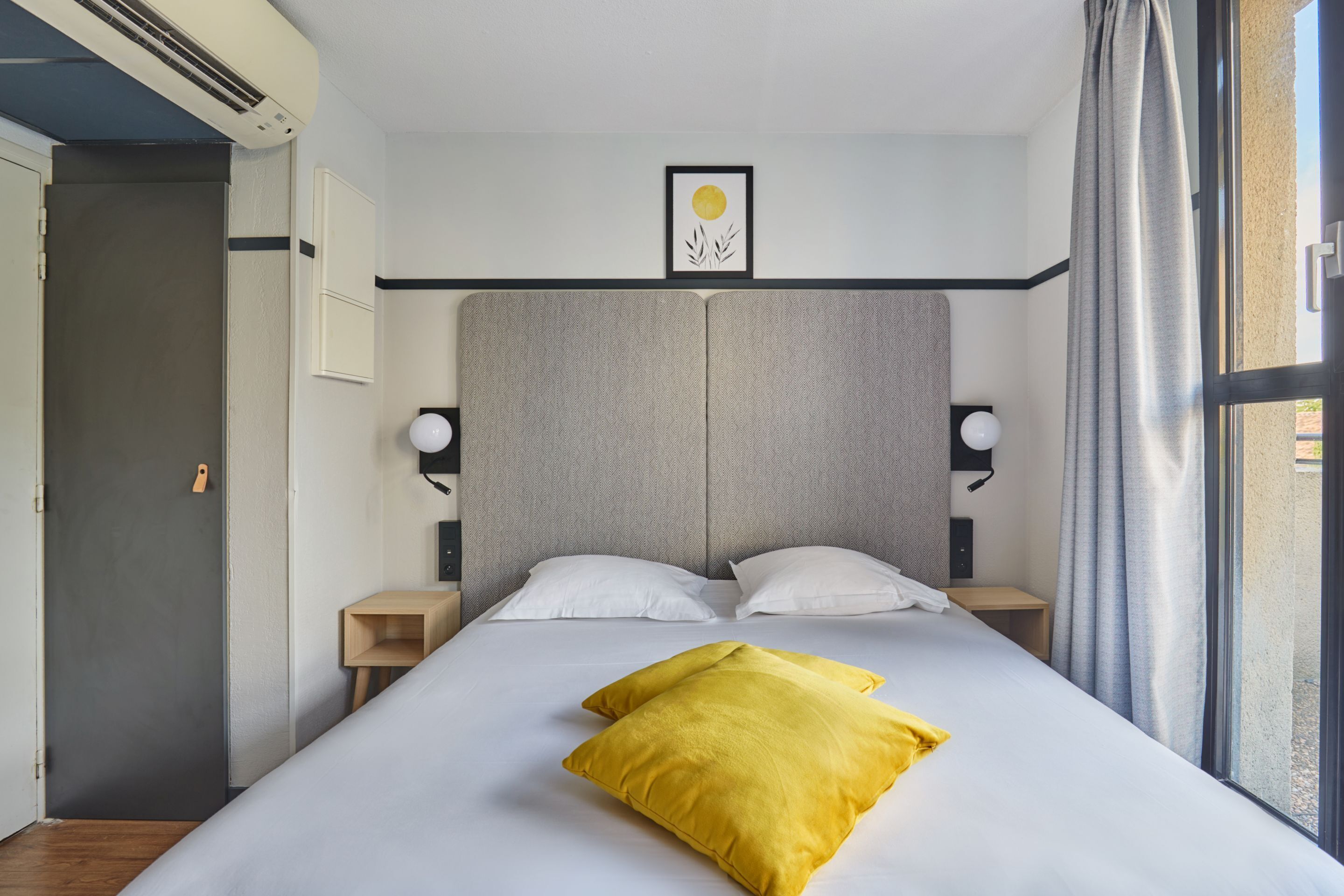 Ein modernes Hotelzimmer mit einem großen Bett, zwei Nachttischen, einer Kopfteil und einem Fenster mit Vorhängen.
