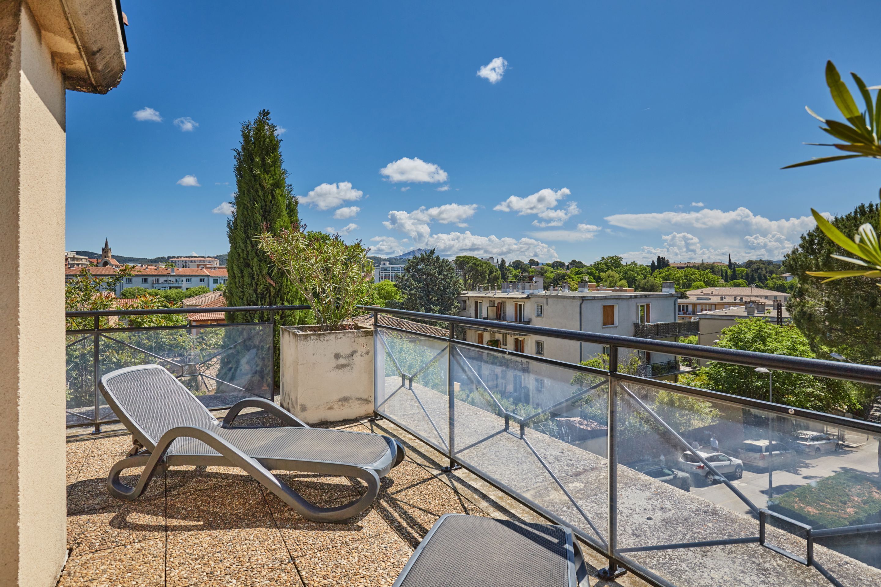 A balcony with two lounge chairs, a clear view of the cityscape, and a glass railing.