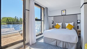 Ein modernes Hotelzimmer mit einem großen Bett, zwei Nachttischen und Blick auf eine Dachterrasse.