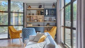 Ein modernes Wohnzimmer mit großem Fenster, einer Couch, zwei Sesseln und einer eingebauten Bücherwand.