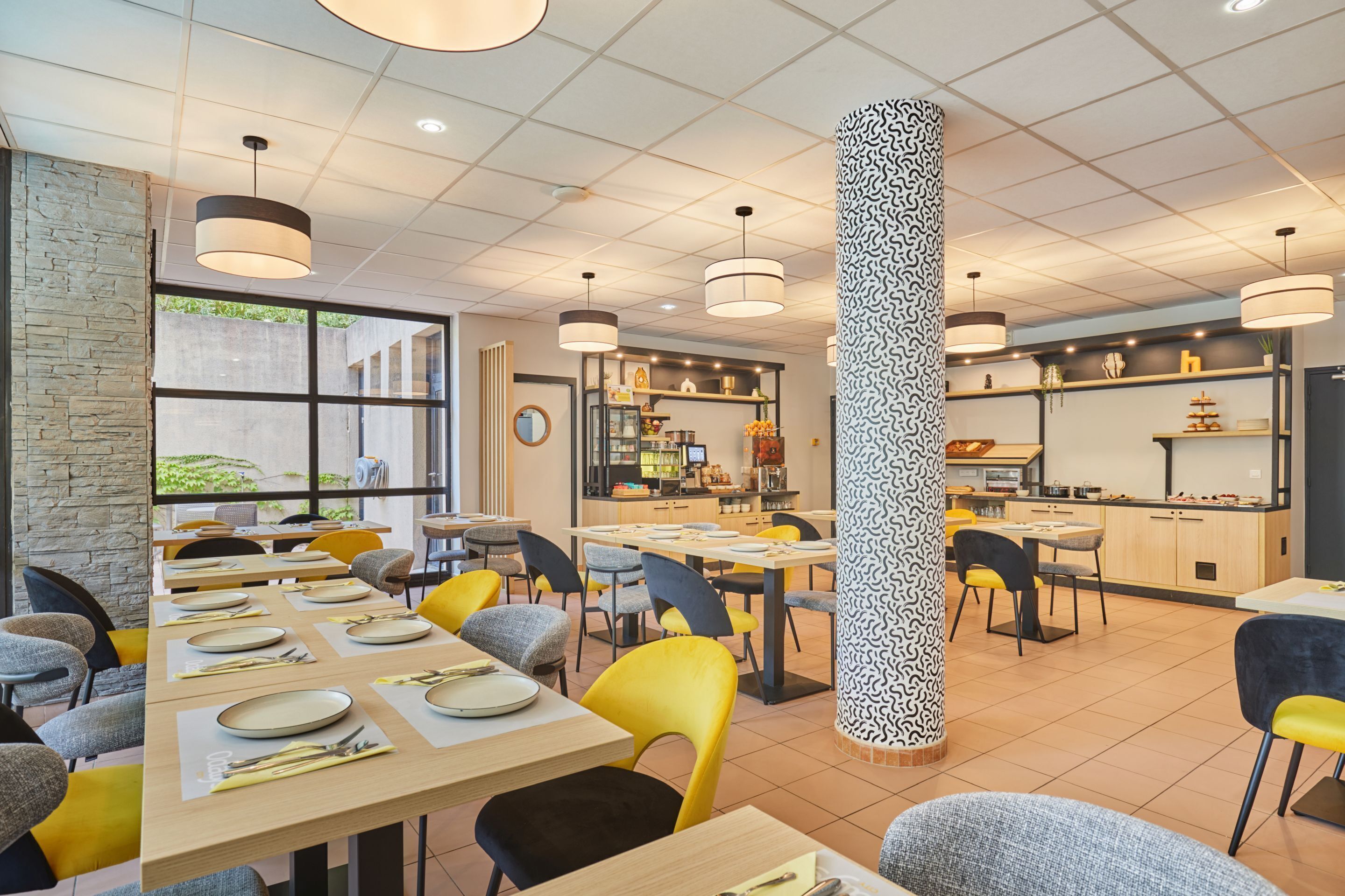 A modern restaurant with multiple dining areas, a central pillar with a unique pattern, and a visible kitchen area.