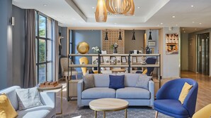 Una sala moderna con sofá, sillones y una mesa de centro. Se observan luces colgantes, una estantería y un panel decorativo en la pared.