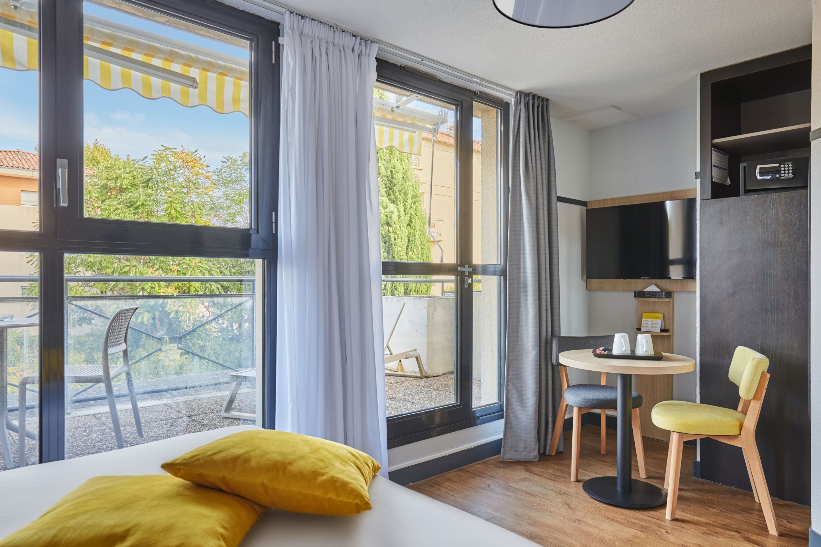 Habitación de hotel con cama, una pequeña mesa con sillas, televisión y balcón con mobiliario exterior.