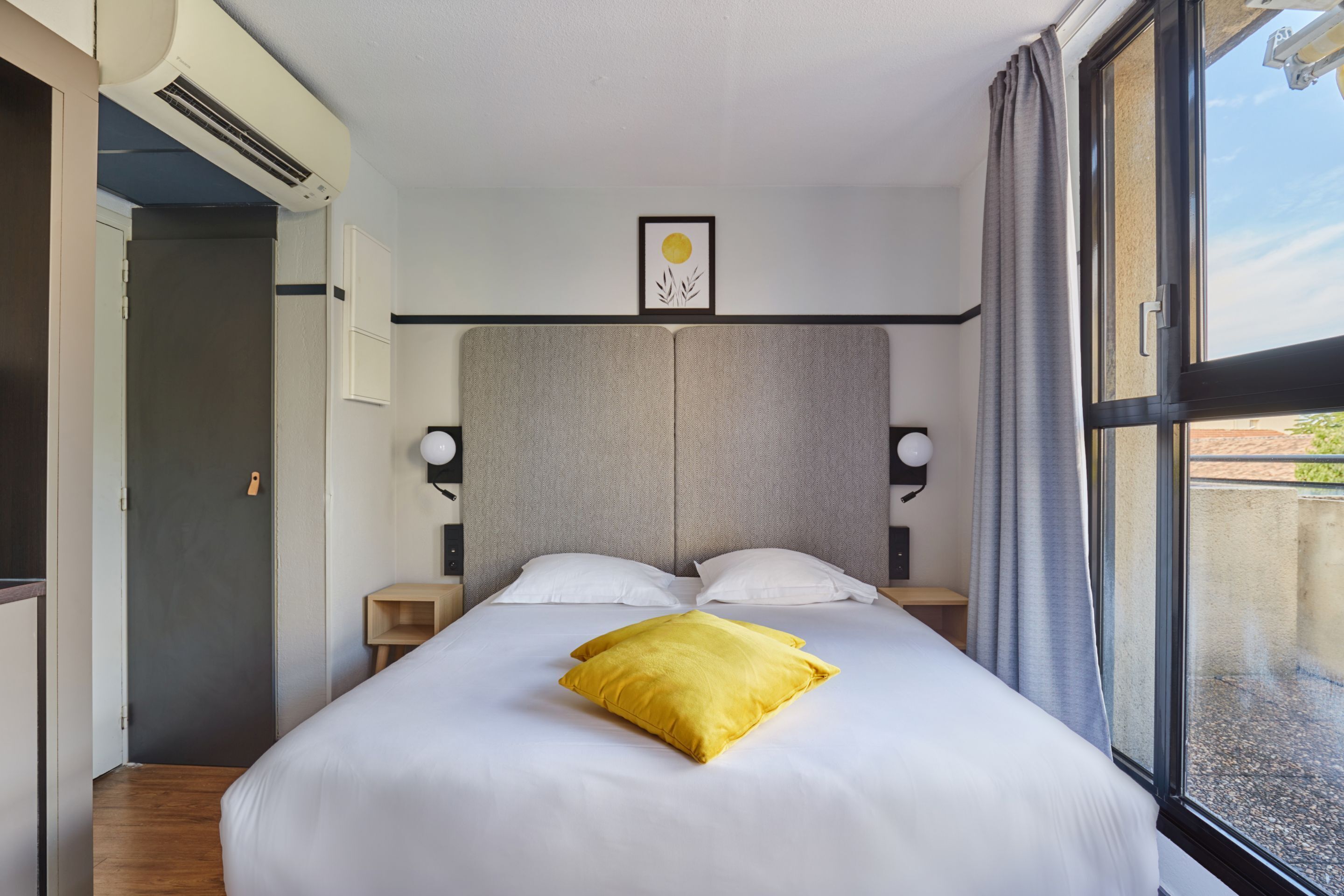 Una habitación de hotel moderna con una cama grande, una mesita de noche y aire acondicionado de pared.
