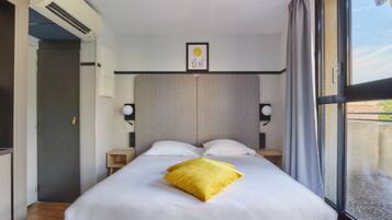 Una habitación de hotel moderna con una cama grande, una mesita de noche y aire acondicionado de pared.