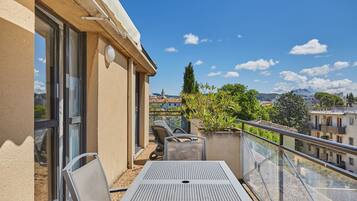 Een balkon met een tafel en stoelen, met uitzicht op een stadsgezicht met gebouwen en een berg in de verte.