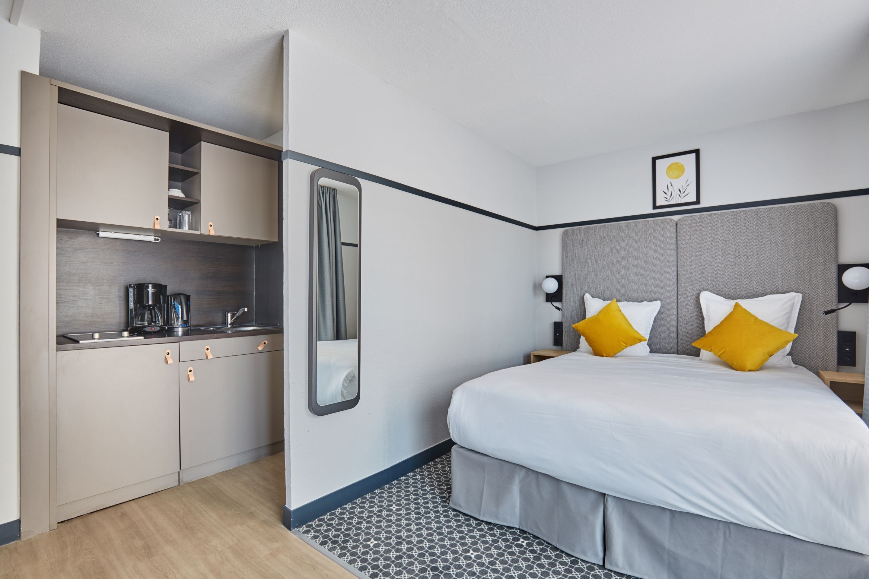 Ein modernes Hotelzimmer mit einer Küchenzeile, einem großen Bett mit zwei Kissen und einem kleinen Nachttisch.