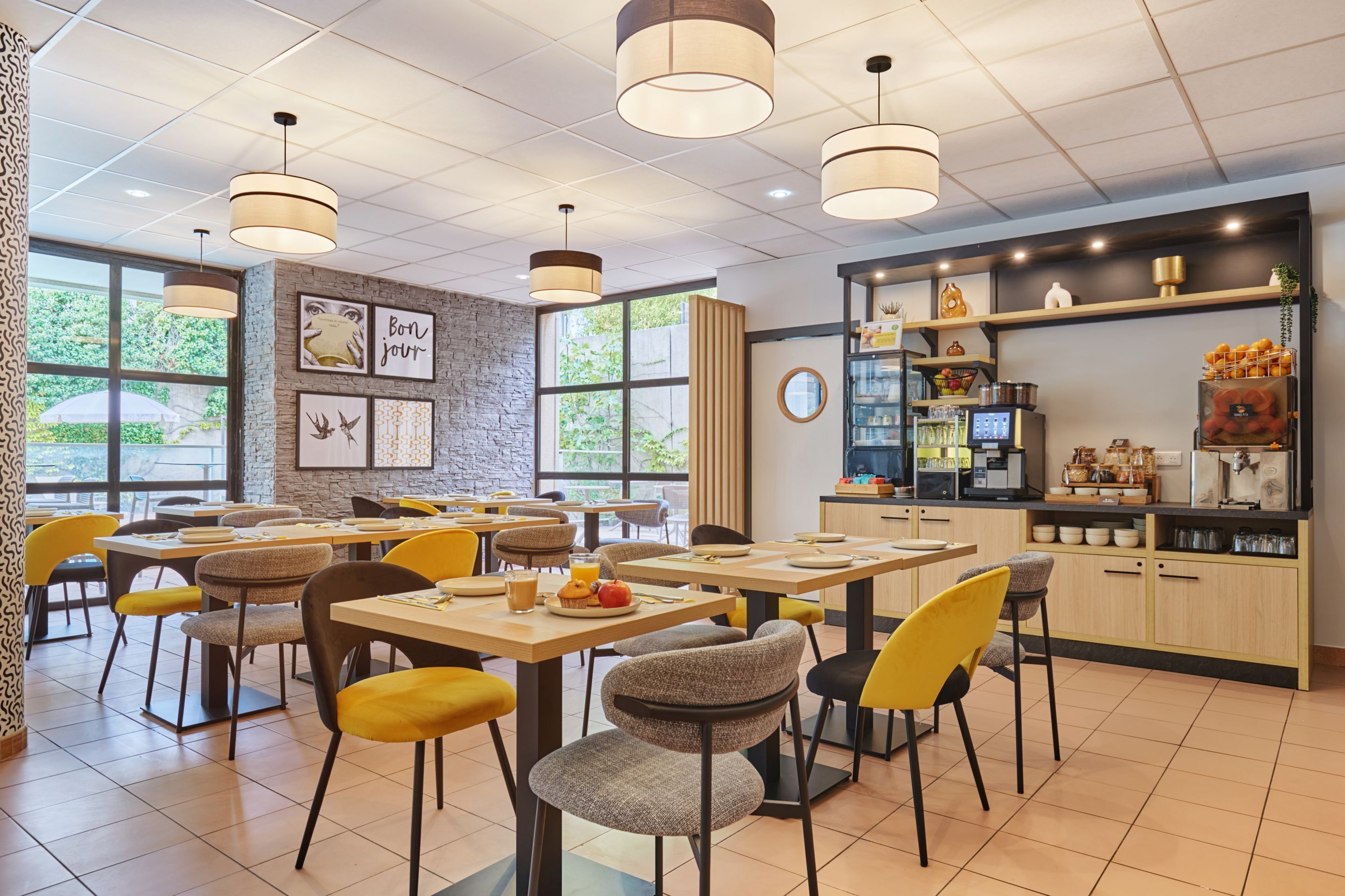 A modern cafe with multiple tables and chairs, a coffee bar, and large windows offering a view of the outdoors.