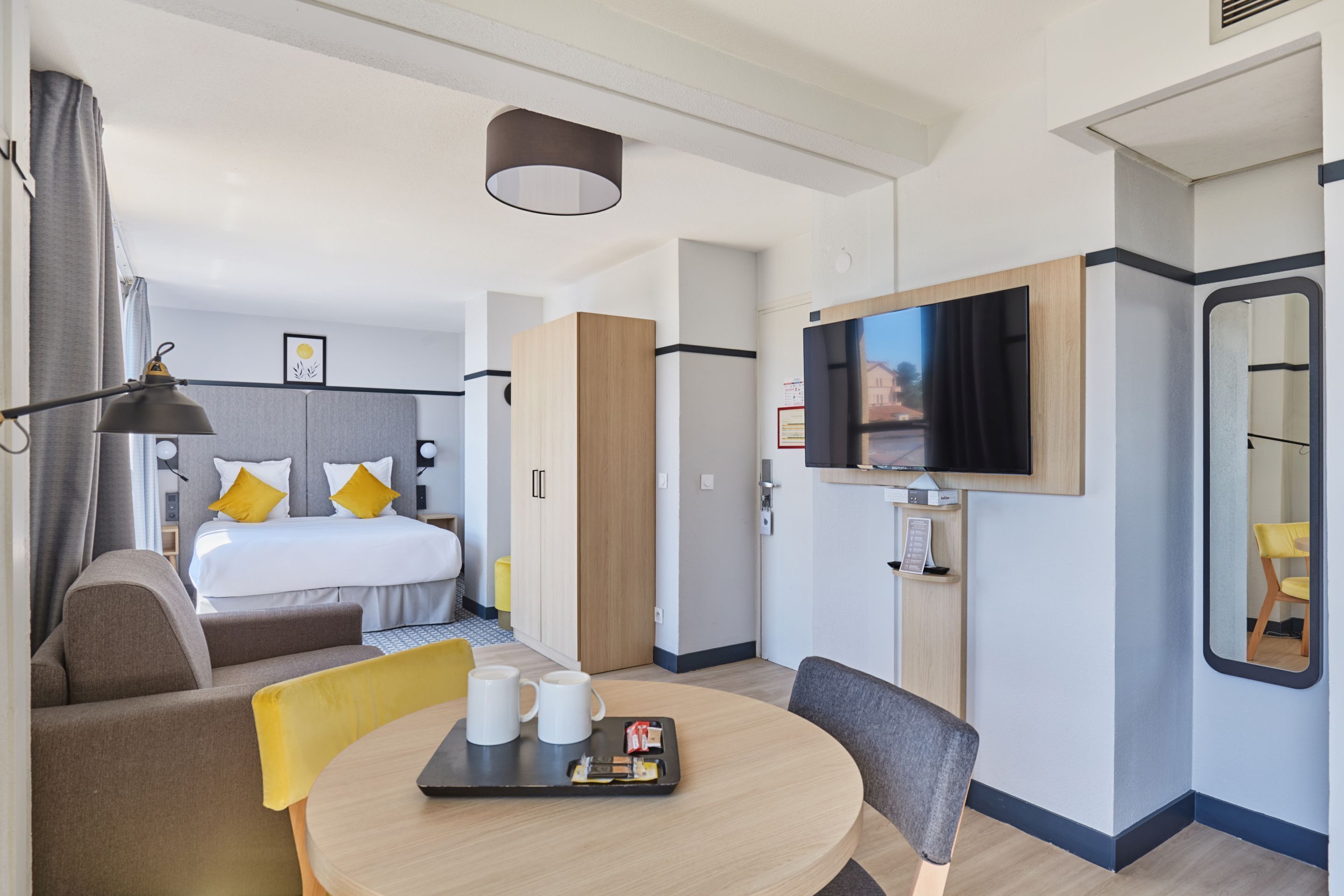 Una habitación de hotel moderna con cama, televisión, zona de comedor con mesa y sillas, y pequeña cocina.