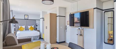 Una habitación de hotel moderna con cama, televisión, zona de comedor con mesa y sillas, y pequeña cocina.