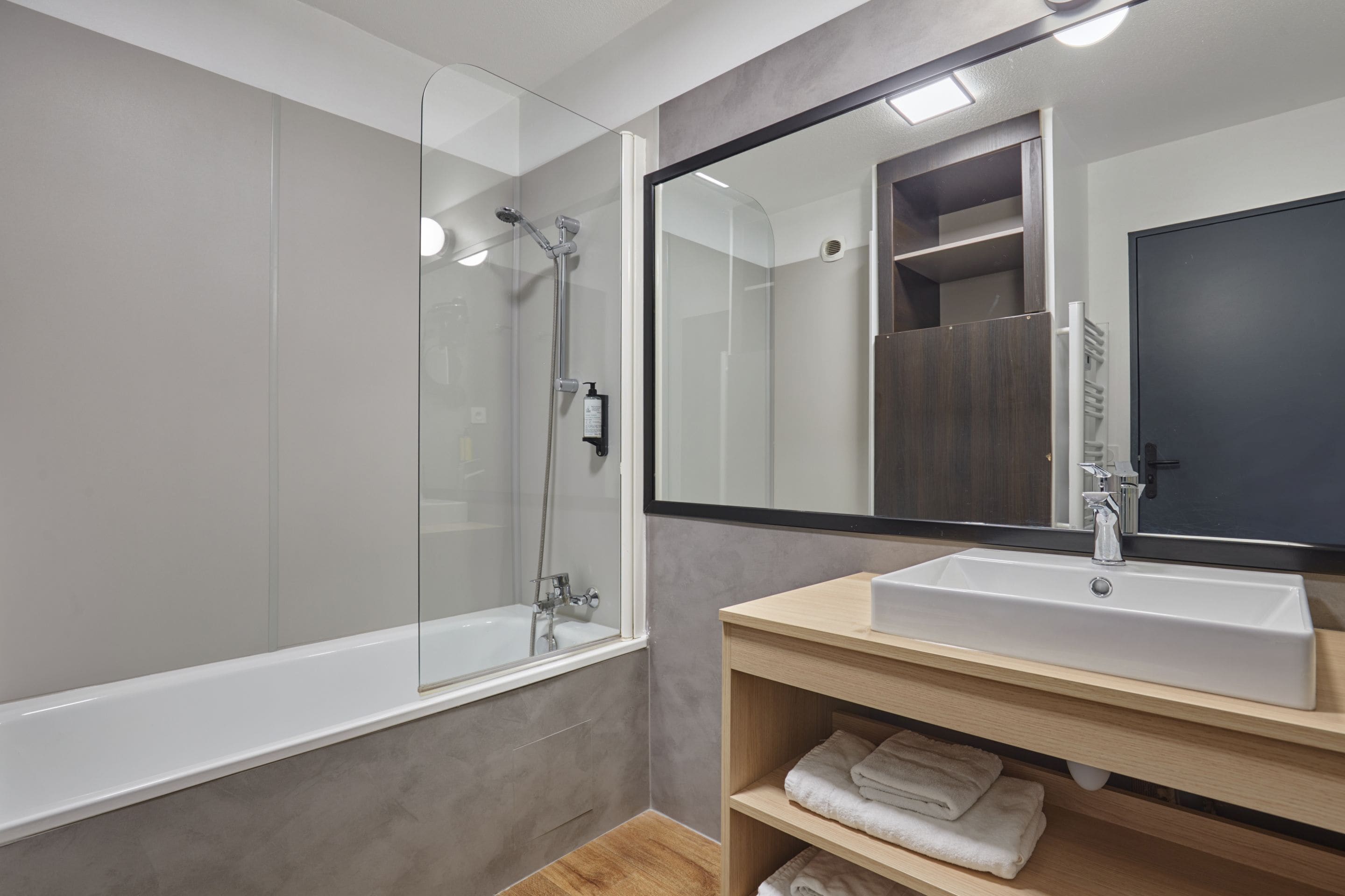 A modern bathroom with a glass-enclosed shower, a white sink, and a large mirror.