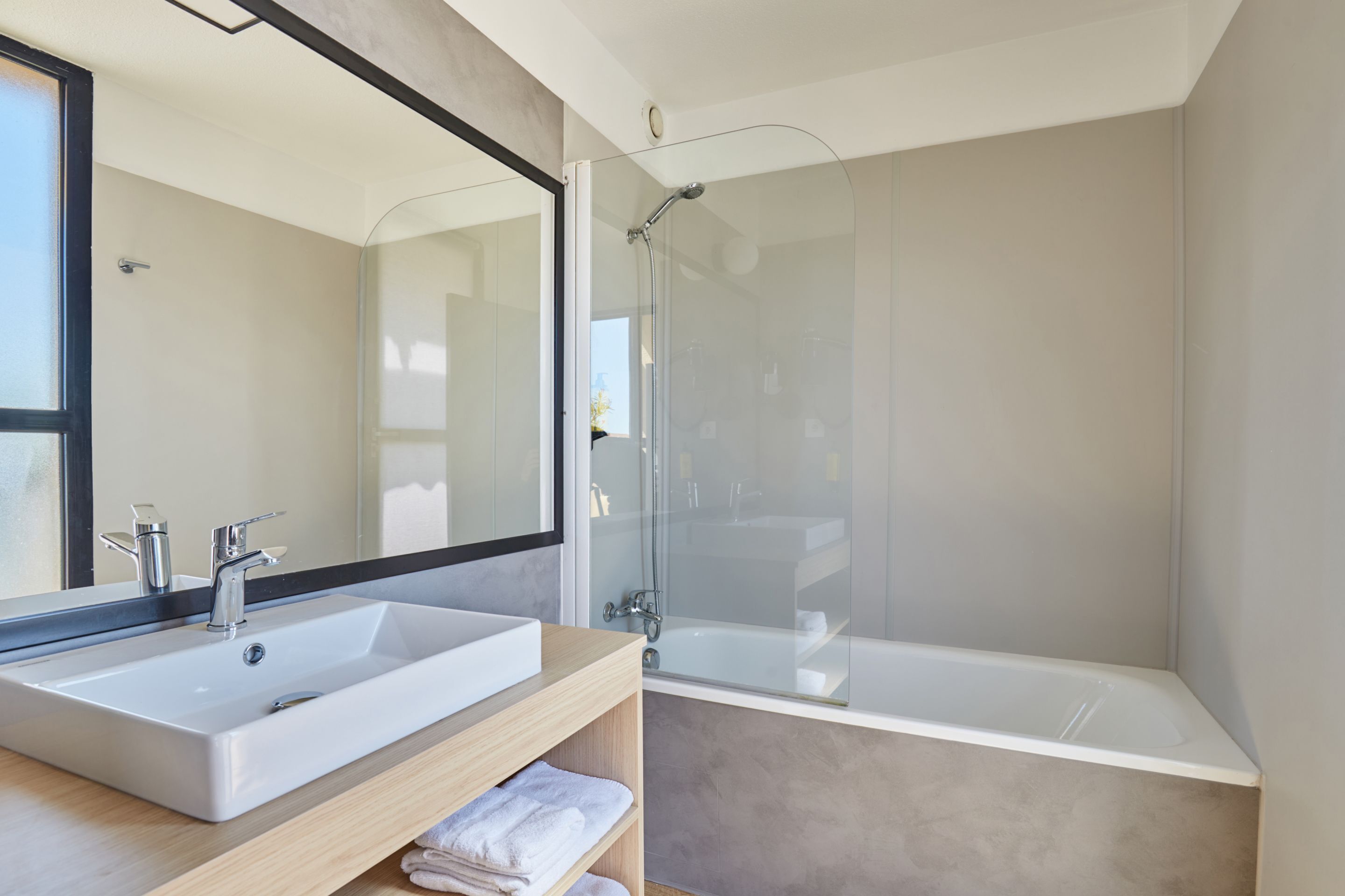 Un baño moderno con un espejo grande, un lavamanos blanco, una bañera y un box de ducha de vidrio.