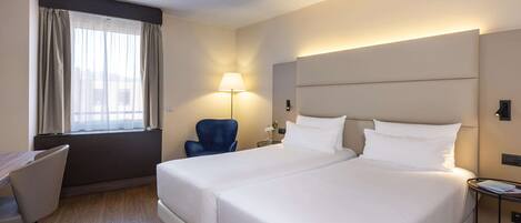 A hotel room with two beds, a desk, a chair, a lamp, and a window with curtains.