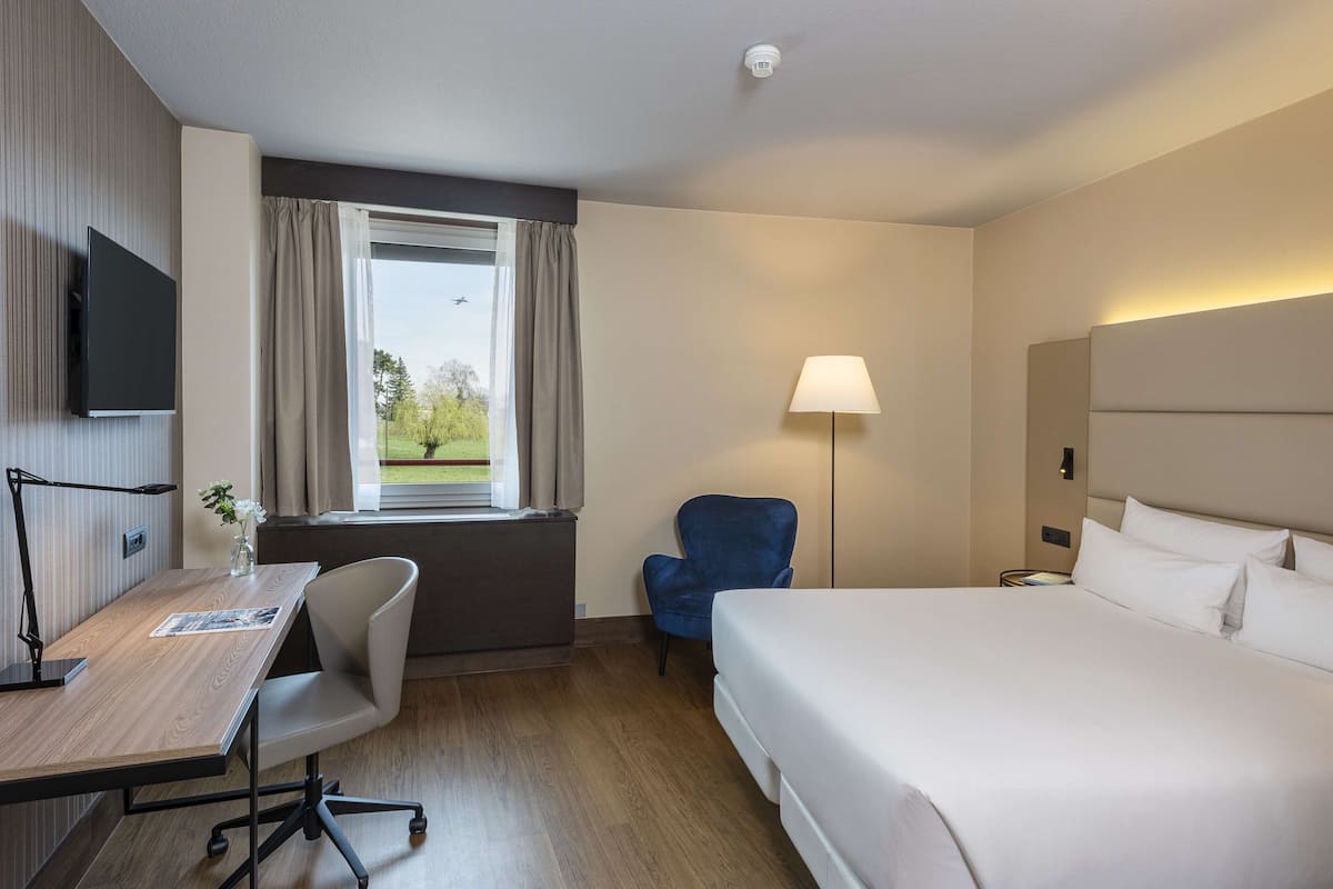 Una habitación de hotel con una cama, un escritorio con una silla, una lámpara y un televisor.