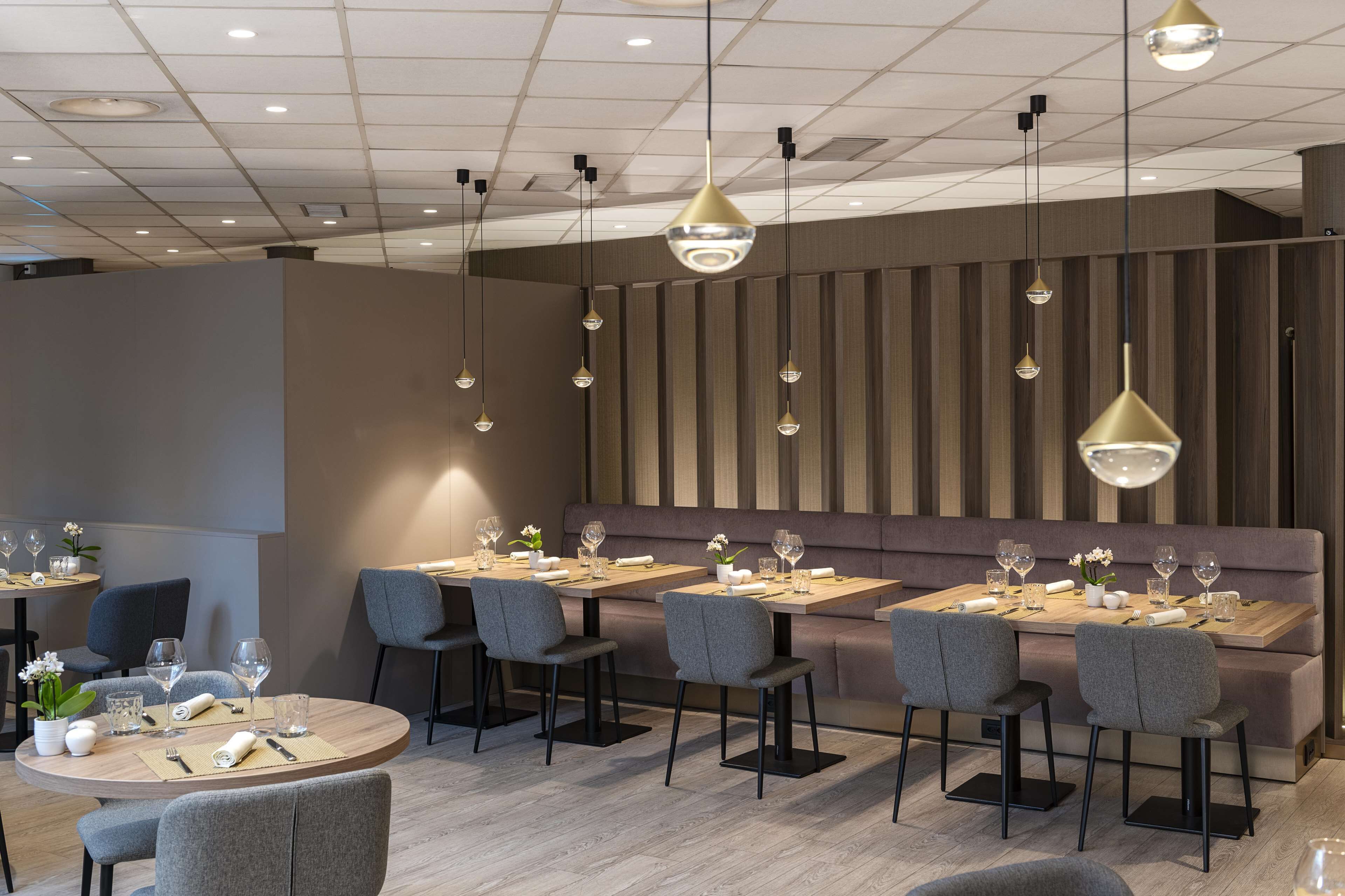 A modern dining area with round tables, grey upholstered chairs, and pendant lighting.