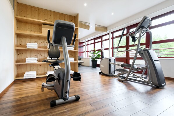 Un gimnasio con equipo de ejercicio, estantes de madera con toallas y ventanas amplias.
