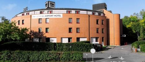 The NH Geneva Airport Hotel with a brick facade, multiple windows, and a sign indicating a stop sign ahead.