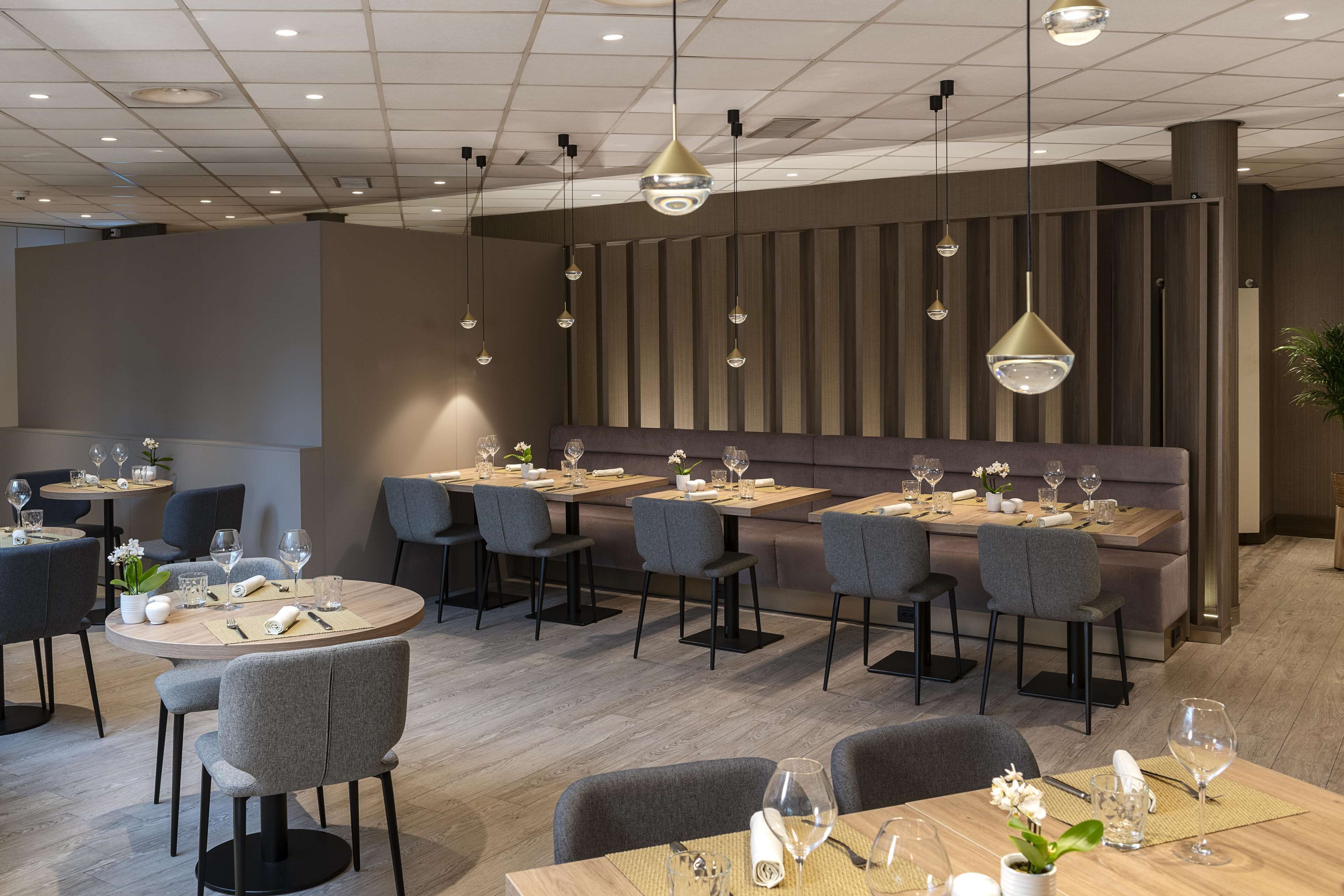 A modern restaurant with round tables, grey upholstered chairs, and pendant lighting.