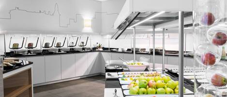 A modern buffet setup with various food items and a city skyline mural on the wall.