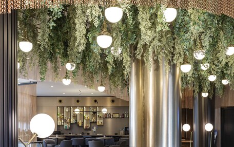 A modern lounge area with a central fire feature, seating arrangements, and hanging greenery.