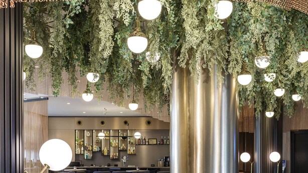 Un espacio lounge moderno con una chimenea central, disposiciones para sentarse y plantas colgantes.