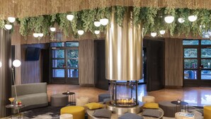 Un espacio lounge moderno con una chimenea central, distribución de asientos y grandes ventanales con vistas.
