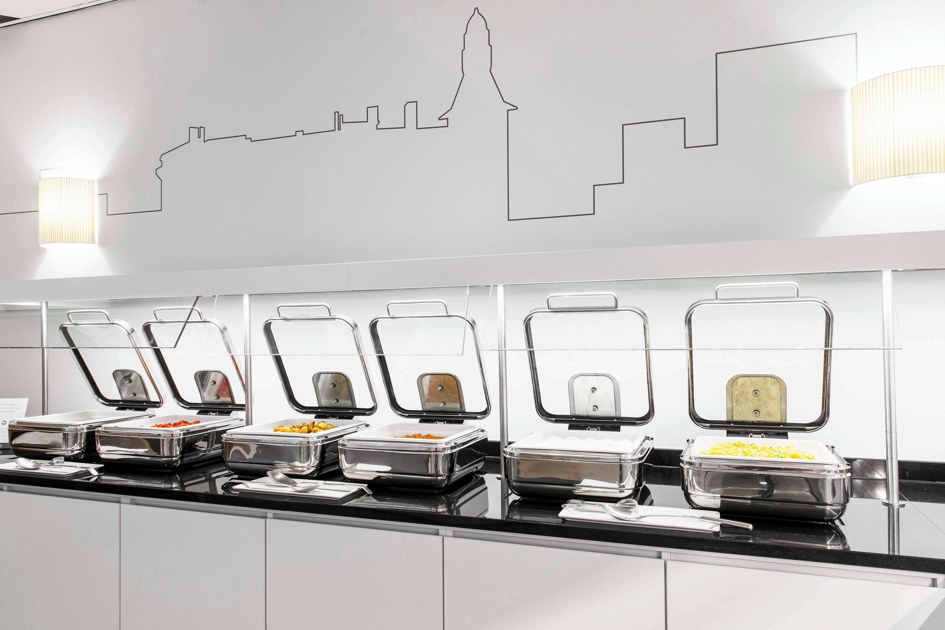 Un buffet avec différents plats présentés dans des récipients et une fresque représentant le paysage urbain sur le mur.